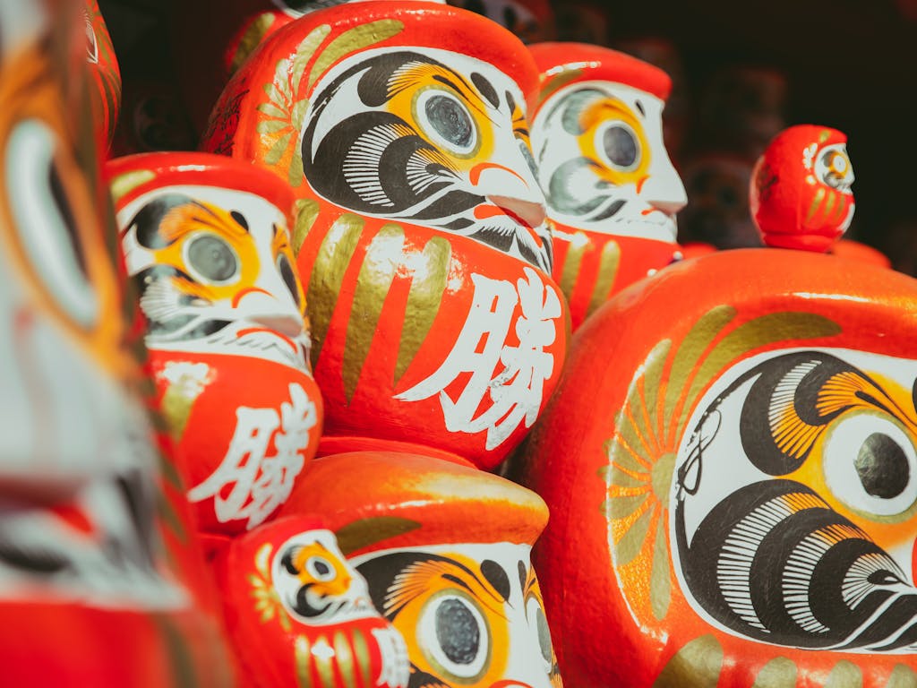 Collection of traditional Japanese red painted daruma dolls depicting bearded man stacked together on local market on street in city